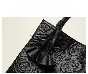 Dettaglio borsa in pelle nera con goffratura a rose e ciondolo a forma di fiore