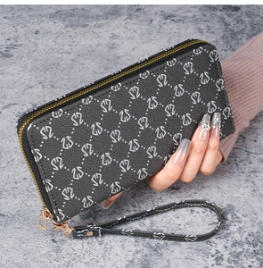 Détail d'une pochette longue noire avec monogramme argenté et fermeture éclair dorée