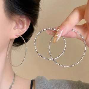 Close-up of textured silver hoop earrings with a twisted design worn by a model