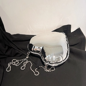 Detail view of heart-shaped silver metallic mini bag with fluid texture on black fabric