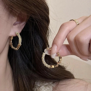 Macro detail of textured gold hoop earrings with matte and square link pattern surfaces