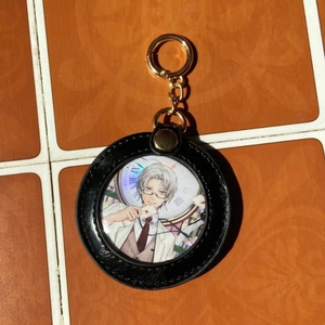 Ronde anime sleutelhanger met zwarte kunstlederen rand en gouden ring op tegels