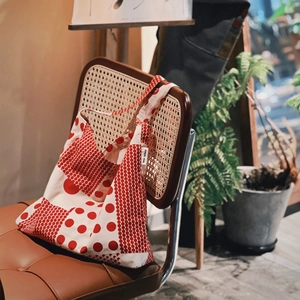 Sac bandoulière en toile rétro à pois rouges suspendu sur une chaise en rotin