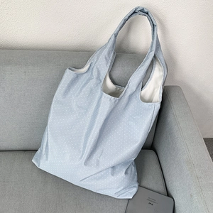 Close-up of a light blue polka dot tote bag placed on a grey sofa with an iPad for scale