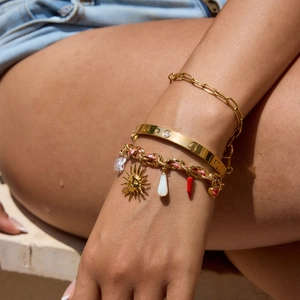 Close-up of stacked gold-plated bracelets featuring sun and chili charms on a woven cord