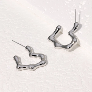 Macro shot of silver wave-shaped geometric earrings on a minimalist white texture