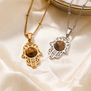 Hamsa hand pendants in gold and silver with tiger eye stone on silk background