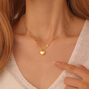 Close-up of golden heart pendant necklace with Love engraving worn by a female model