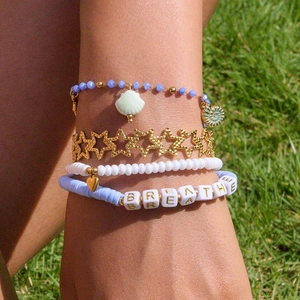 Détail de bracelets superposés en perles or et bleues avec breloque coquillage
