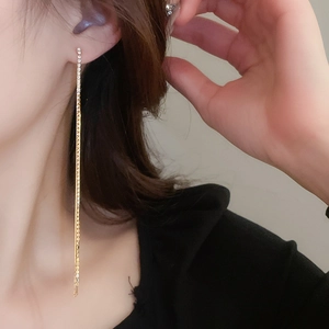 Close-up of golden tassel earrings with rhinestones worn by a model to show long drop effect