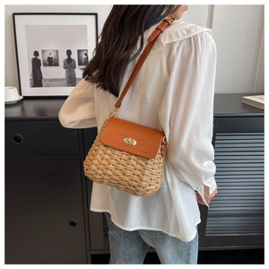 Close-up of handmade straw crossbody bag featuring brown leather flap and golden twist lock