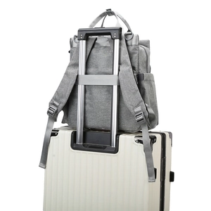 Grey waterproof mommy backpack with luggage strap fixed on a white suitcase handle