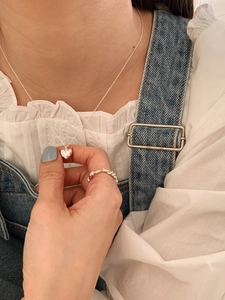 Detail of silver heart pendant necklace and twisted rope ring on female model