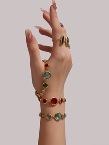 Detailed close-up of 18K gold hand chain and rings with multi-color Czech glass gemstones
