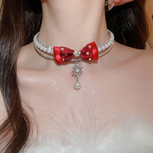 Detail of a multi-layer pearl necklace with a red bow and snowflake pendant on a model