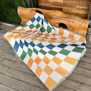 Close-up of colorful geometric diamond pattern knit blanket with fringe edge on wooden stool