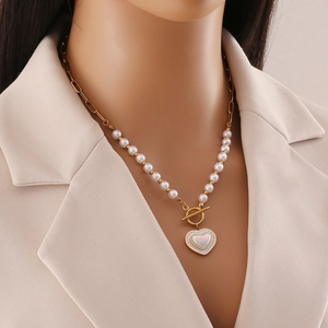Golden pearl necklace with heart pendant and T-bar clasp worn with beige blazer