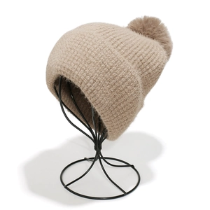 Close-up of beige knit beanie featuring a fluffy faux fur pompom and waffle texture
