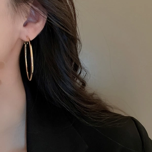 Close-up of a model wearing large minimalist golden metal hoop earrings for women