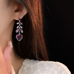 Gros plan d'un modèle portant une boucle d'oreille en strass violet en forme de cœur