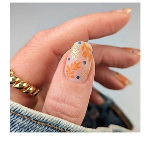 Macro shot of press-on nails featuring orange leaf patterns and blue dot accents