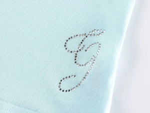Close-up of sparkling rhinestone J letter on light blue ribbed knit loungewear fabric