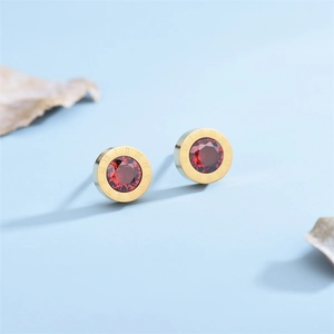 Macro shot of gold Roman numeral stud earrings featuring a faceted red round gemstone