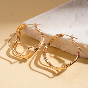 Macro detail of geometric wavy gold earrings showcasing high-shine metallic texture