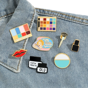 Set of 8 colorful enamel pins featuring makeup shapes on blue denim fabric collar