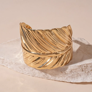 Detailed view of golden leaf textured feather cuff bracelet on a white stone background