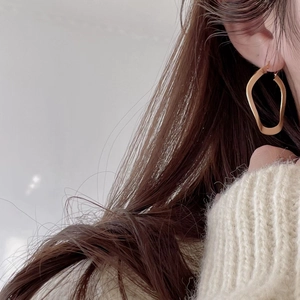 Elegant gold irregular hoop earrings worn by a model in a minimalist lifestyle setting