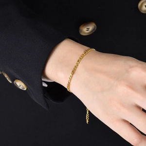 Classic 18K gold Figaro chain bracelet styled on a wrist with a black blazer background