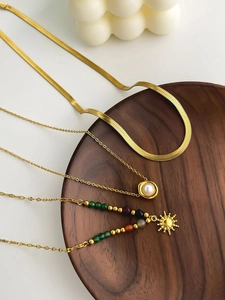 Detailed set of 18K gold plated necklaces with sun charm and pearl pendant on wood