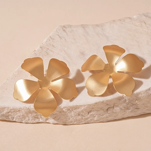 Close-up of matte gold flower earrings with a minimalist five-petal metallic design