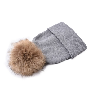 Dettaglio del berretto in maglia grigio chiaro con un grande pompon marrone in pelliccia