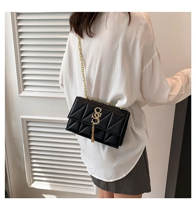 Detail of black quilted chain bag featuring gold SS logo and elegant tassel pendant