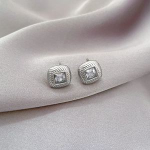 Macro detail of silver square zircon stud earrings on purple silk background