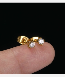Macro shot of 18K gold minimalist stud earring with clear zircon on a finger