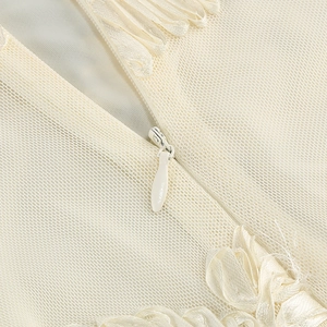 Detailed macro view of invisible zipper on cream halter dress with mesh and satin textures
