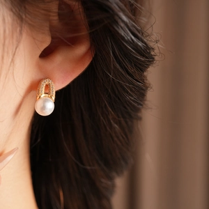 Gros plan de boucles d'oreilles dorées en U avec zircons et perle blanche sur modèle