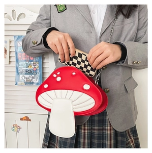 Detail showing red mushroom crossbody bag with chain strap being held by a model