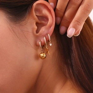 Detail of 18K gold plated hoop earrings with star, heart and ball charms on model ear