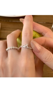Detailed view of silver bow and lace flower pearl rings worn on a person's fingers