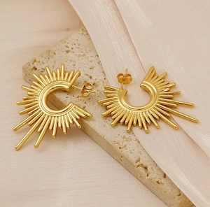 Detail of irregular geometric sunburst earrings in gold plating on a stone texture base