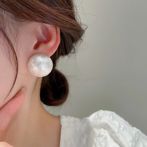 Close-up of elegant white round faux pearl earrings with a textured surface on a model