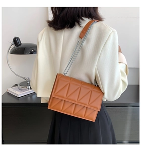 Detail of a brown quilted crossbody bag with silver chain strap shown on a model