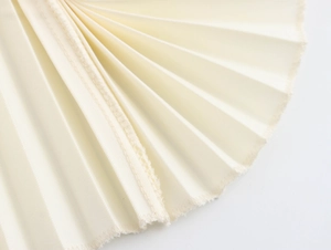 Close-up detail of cream white pleated fabric with elegant textured wrinkles and raw edges