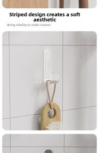 Detail of transparent striped adhesive hook holding a brush on a white tiled wall