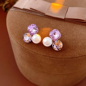 Macro view of triangle pearl stud earrings with purple crystals on brown jewelry box