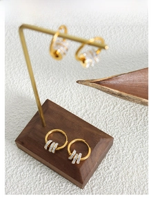 Detailaufnahme goldener Titan-Ohrringe mit glitzerndem Zirkon-Inlay auf einem Holzständer